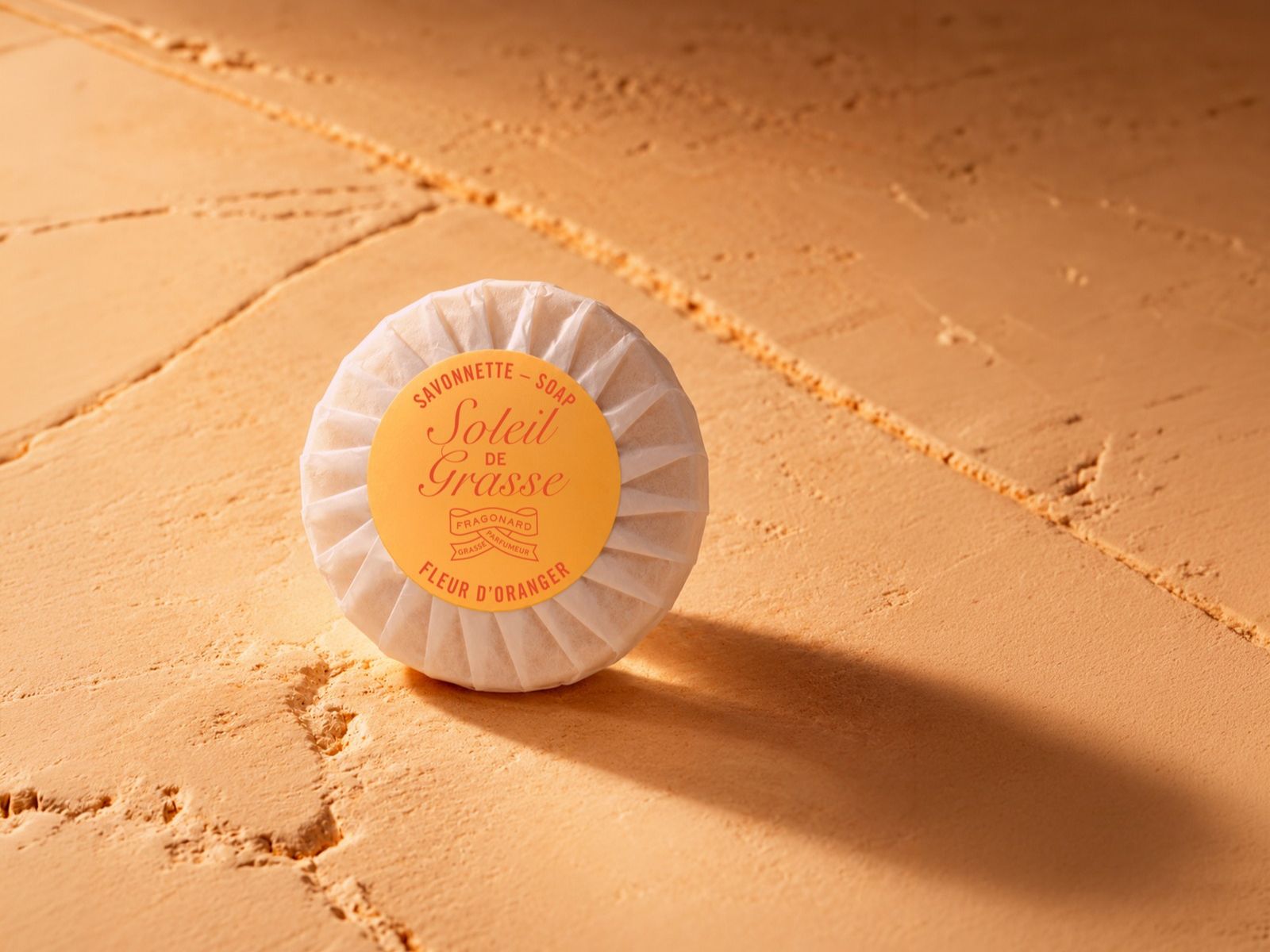 Fragonard Soleil de Grasse orange blossom scented soap wrapped in elegant packaging with a warm sunlit backdrop.